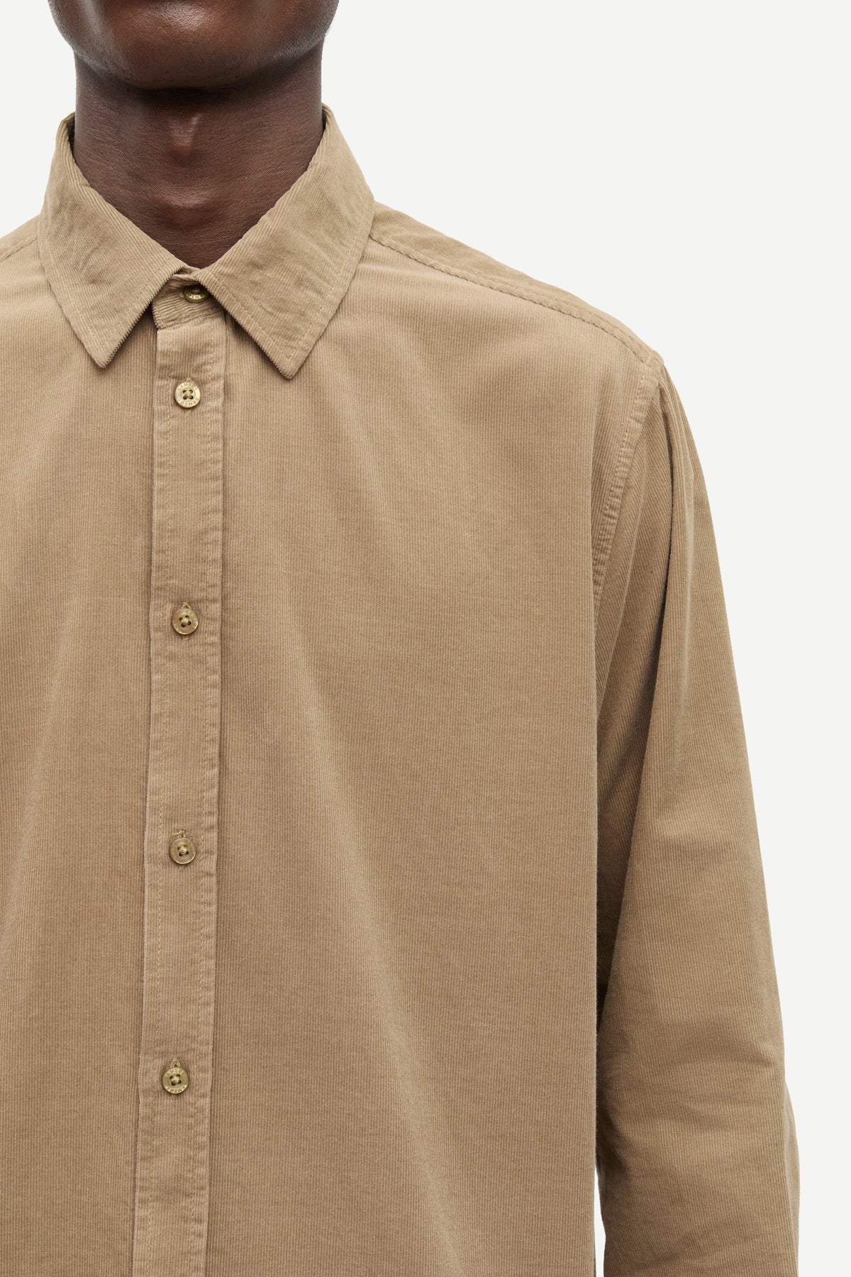 Close-up of a man wearing a tan long-sleeve button-down shirt with a pointed collar and matching buttons, shown against a plain light background.