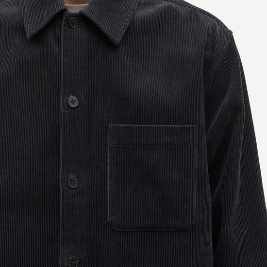 A black long-sleeve quarter-zip pullover sweater hanging on a black hanger against a plain off-white wall. The zipper pull features a small gold-tone monogram logo.