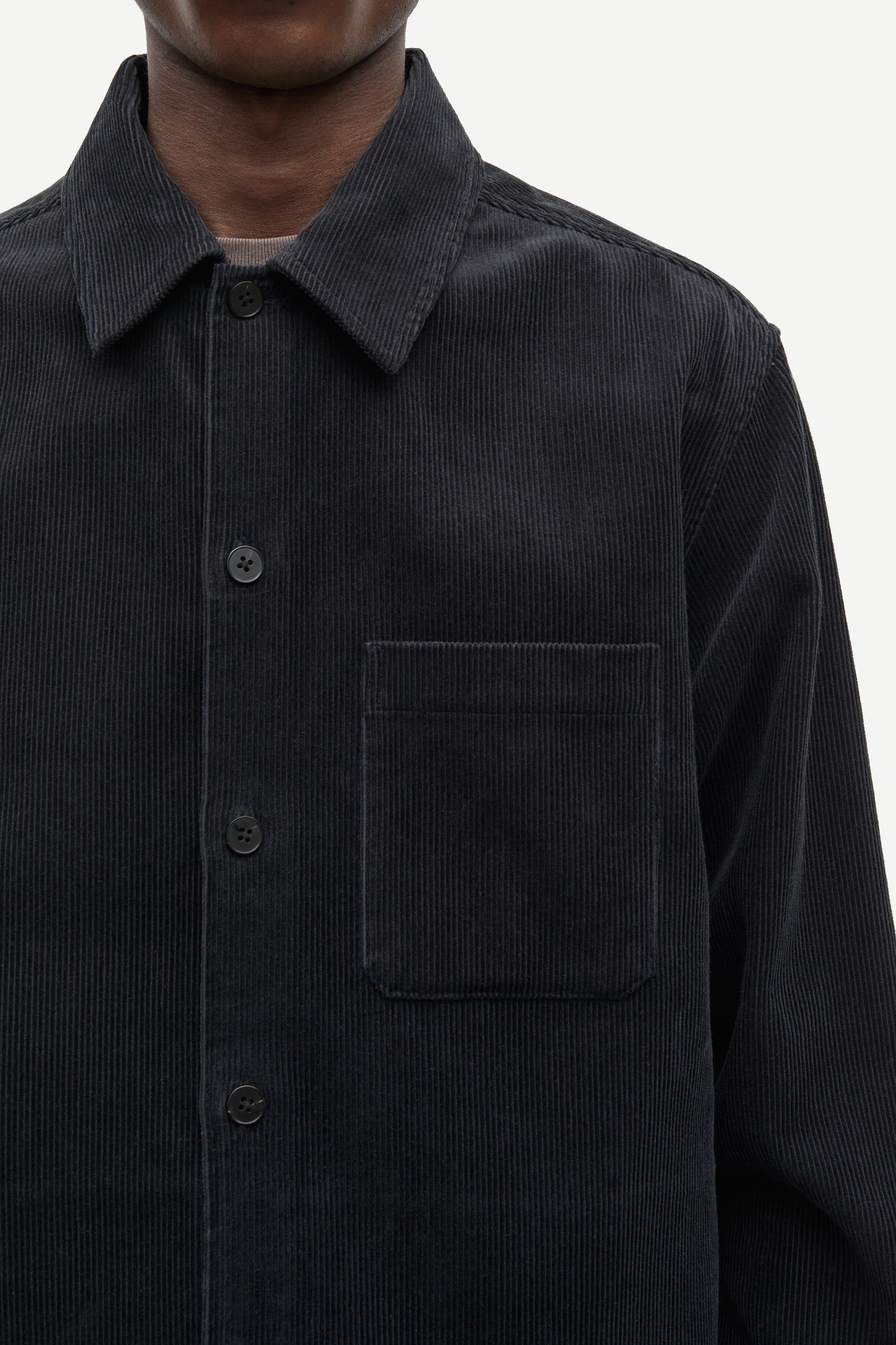 A black long-sleeve quarter-zip pullover sweater hanging on a black hanger against a plain off-white wall. The zipper pull features a small gold-tone monogram logo.