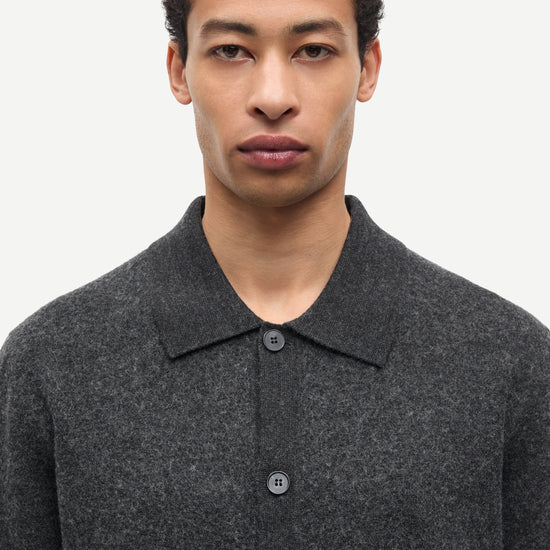 A man wearing a dark gray textured knit polo shirt with a buttoned front, shown from the chest up against a plain light background.