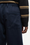Close-up of a person wearing dark navy pants with a back pocket and a black fleece sweater featuring tan stripes.