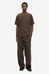 A man modeling a matching brown short-sleeve crewneck t-shirt and wide-leg brown trousers against a light gray studio background.