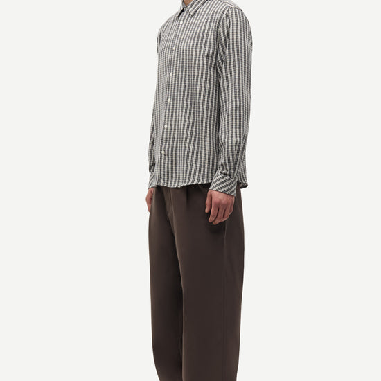 Man wearing a checkered shirt and brown pants on a white background