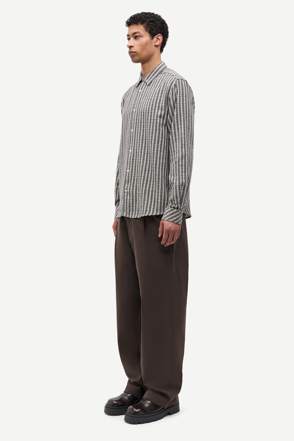 Man wearing a checkered shirt and brown pants on a white background