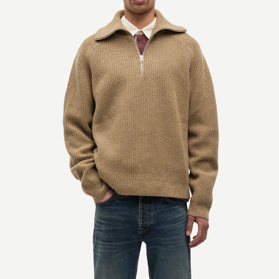 Man wearing a beige half-zip sweater and blue jeans on a white background