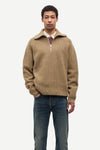 Man wearing a beige half-zip sweater and blue jeans on a white background