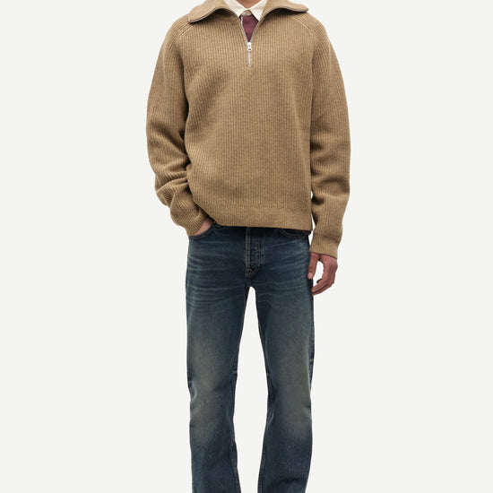 Man wearing a beige half-zip sweater and blue jeans on a white background