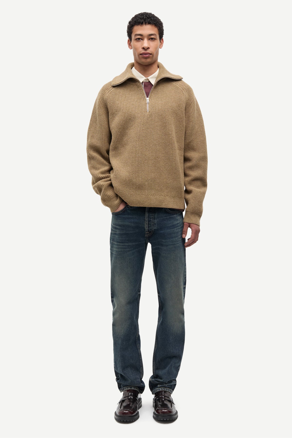 Man wearing a beige half-zip sweater and blue jeans on a white background