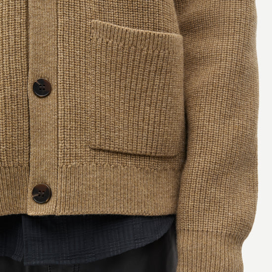 Close-up of a textured brown knit cardigan sweater with dark buttons and a front pocket, worn over a dark shirt and black pants.