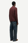 A man shown from the back wearing a dark burgundy knit sweater and wide-leg blue jeans, standing against a plain light gray studio background.