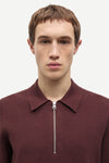 A man wearing a burgundy half-zip knit polo sweater, shown from the chest up against a plain light gray background.