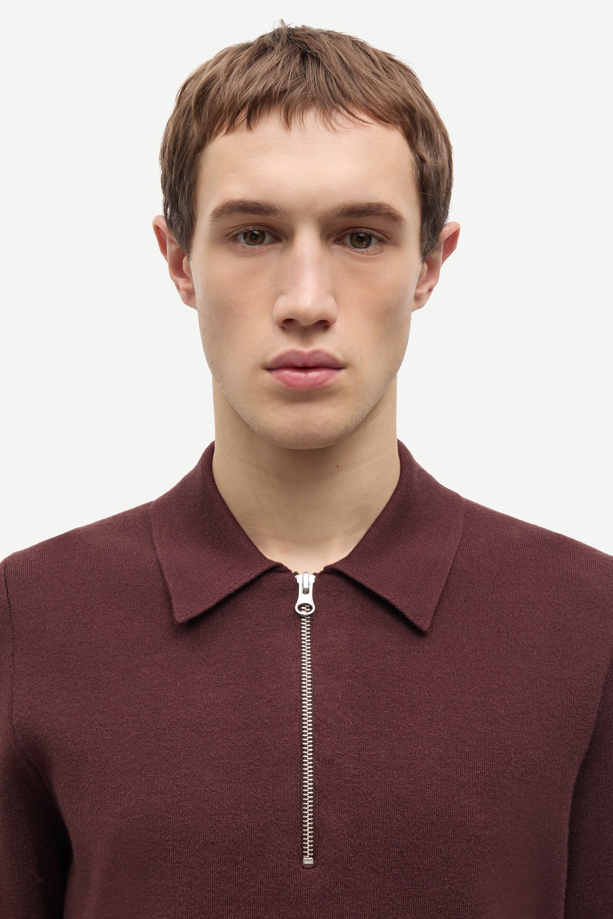 A man wearing a burgundy half-zip knit polo sweater, shown from the chest up against a plain light gray background.