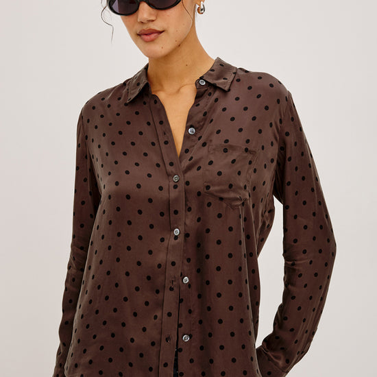 Woman wearing a brown polka dot shirt against a plain background