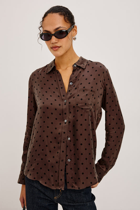Woman wearing a brown polka dot shirt against a plain background
