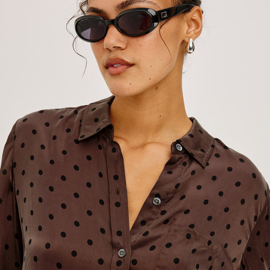 Woman wearing a brown polka dot shirt with sunglasses on a plain background