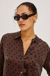 Woman wearing a brown polka dot shirt with sunglasses on a plain background