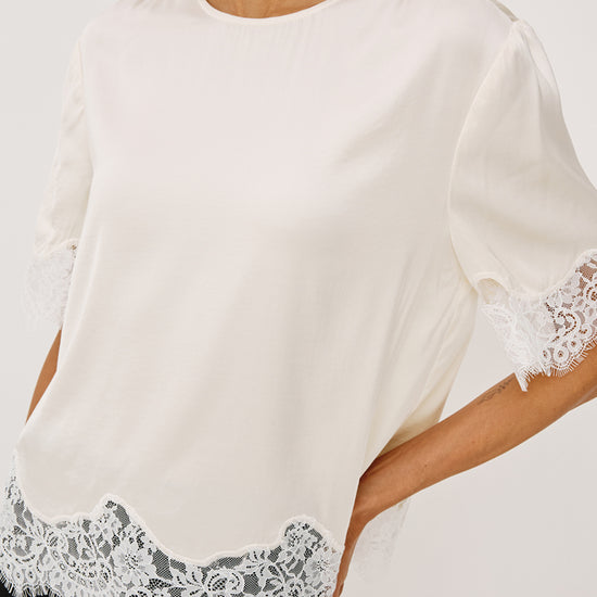 Woman wearing an ivory lace top with black trousers side view