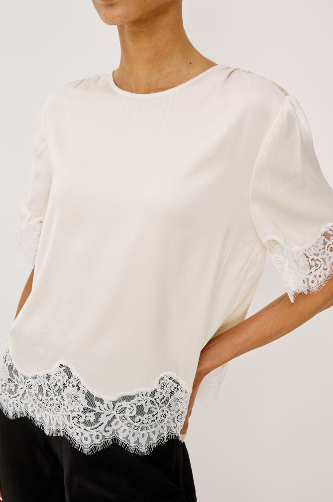 Woman wearing an ivory lace top with black trousers side view