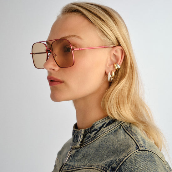 Woman wearing oversized sunglasses and a denim jacket on a plain background
