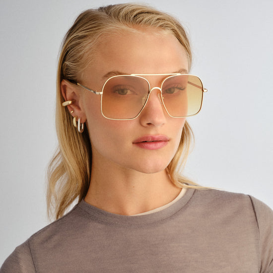 Woman wearing gold-framed sunglasses with a plain background