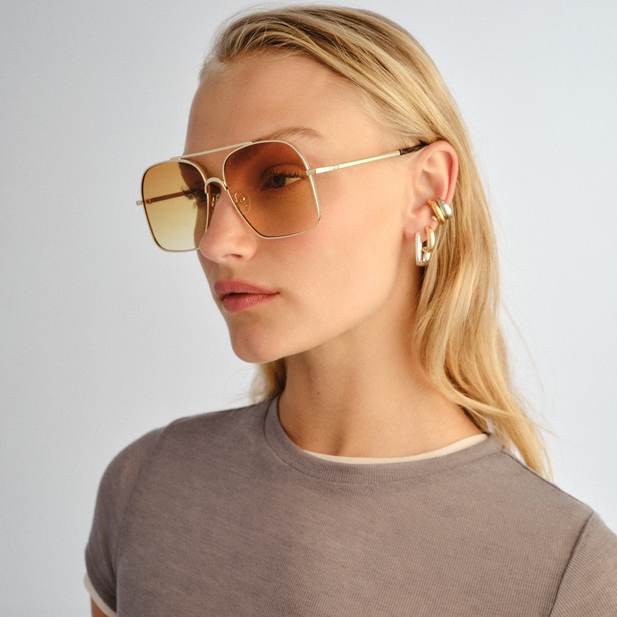 Woman wearing gold sunglasses and earrings on a plain background