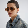 Woman wearing brown sunglasses and a denim jacket on a light gray background