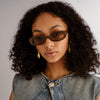 Woman wearing sunglasses and a denim jacket against a neutral background