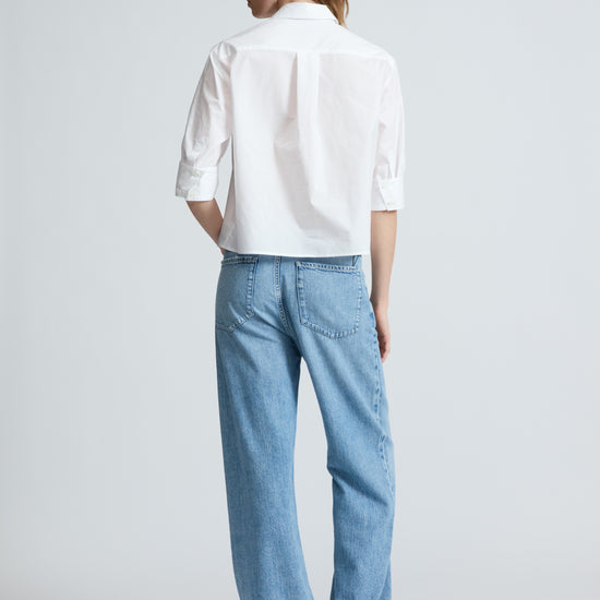 Person wearing a white shirt and light blue jeans on a plain background