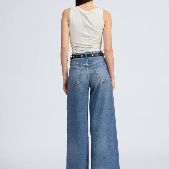 Woman wearing a white sleeveless top and blue jeans on a white background