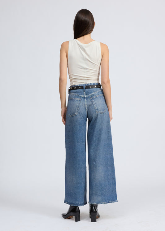 Woman wearing a white sleeveless top and blue jeans on a white background