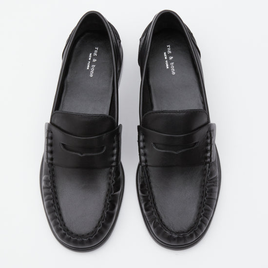 A pair of black leather penny loafers with braided detailing around the sole, photographed from a top-down perspective on a clean white background.
