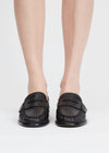 A pair of black leather penny loafers worn by a model, shown from the front against a clean white studio background.