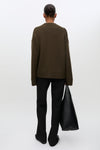 A model shown from the back wearing an oversized dark brown knit sweater, black flared trousers, and holding a large black leather tote bag against a clean white studio background.