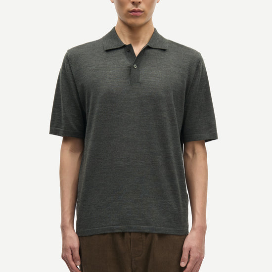 Man wearing a dark green polo shirt and brown pants on a white from Samsoe Samsoe background