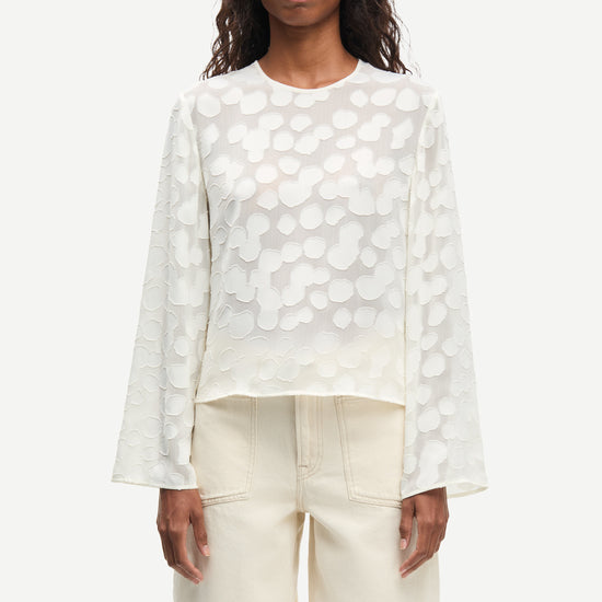 Woman wearing a cream polka dot blouse and cream pants on a white background from Samsoe Samsoe
