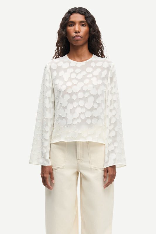 Woman wearing a cream polka dot blouse and cream pants on a white background from Samsoe Samsoe