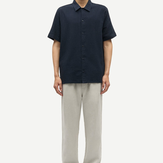 Man wearing a dark blue button-up shirt and light gray pants on a white background