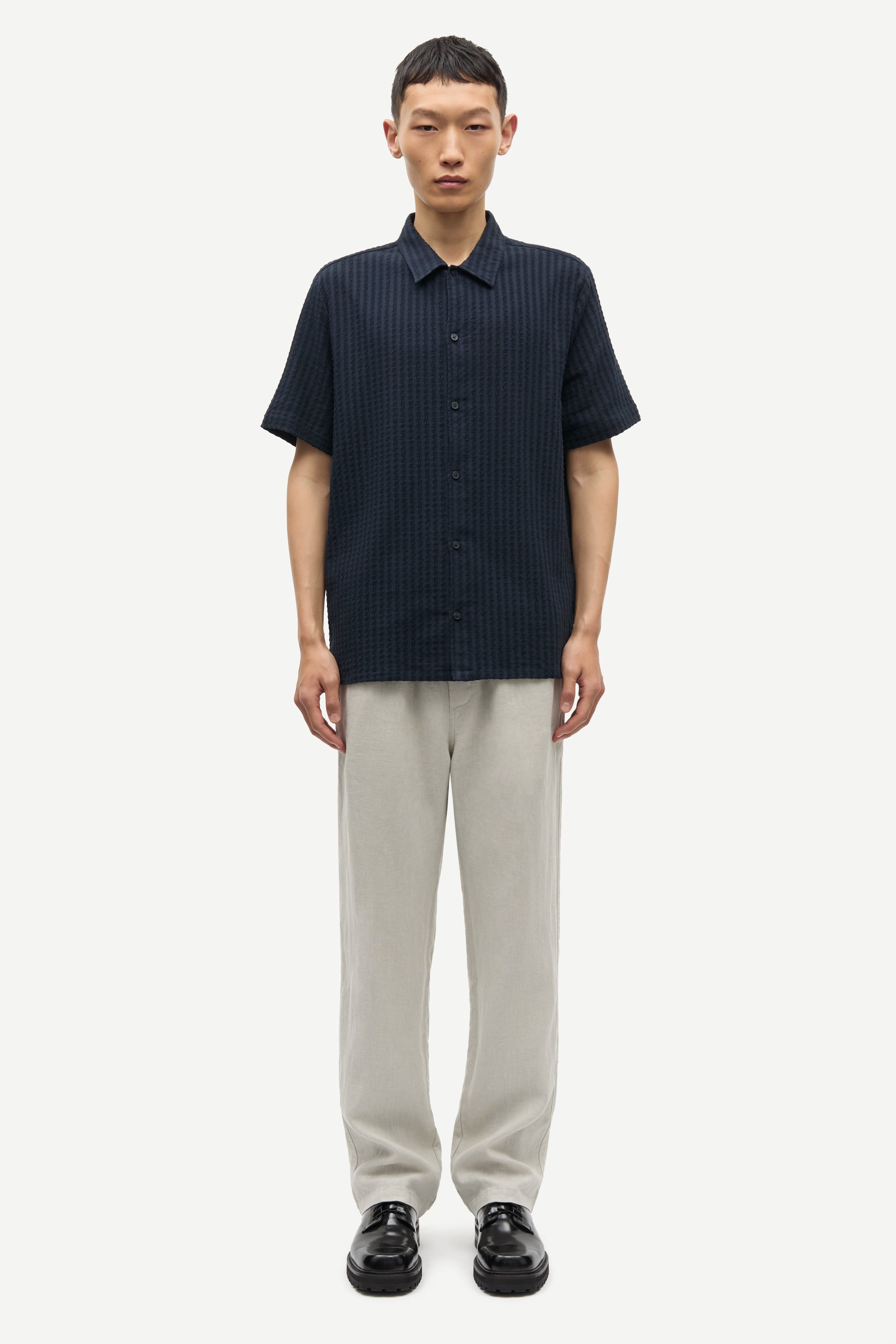 Man wearing a dark blue button-up shirt and light gray pants on a white background