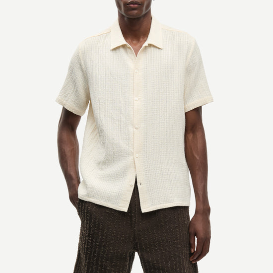 Man wearing a cream short-sleeve shirt and brown shorts on a white background