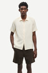 Man wearing a cream short-sleeve shirt and brown shorts on a white background