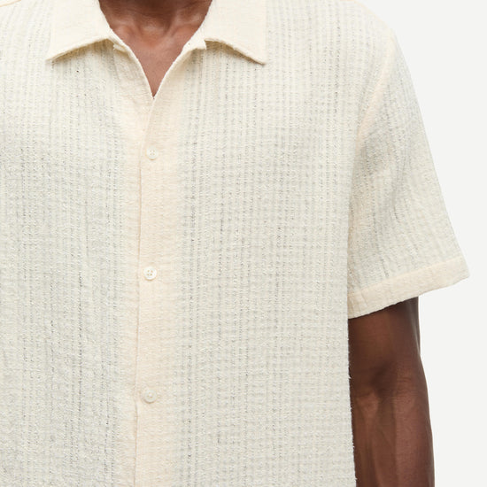 Close-up of a person wearing a textured beige shirt with short sleeves.