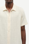 Close-up of a person wearing a textured beige shirt with short sleeves.