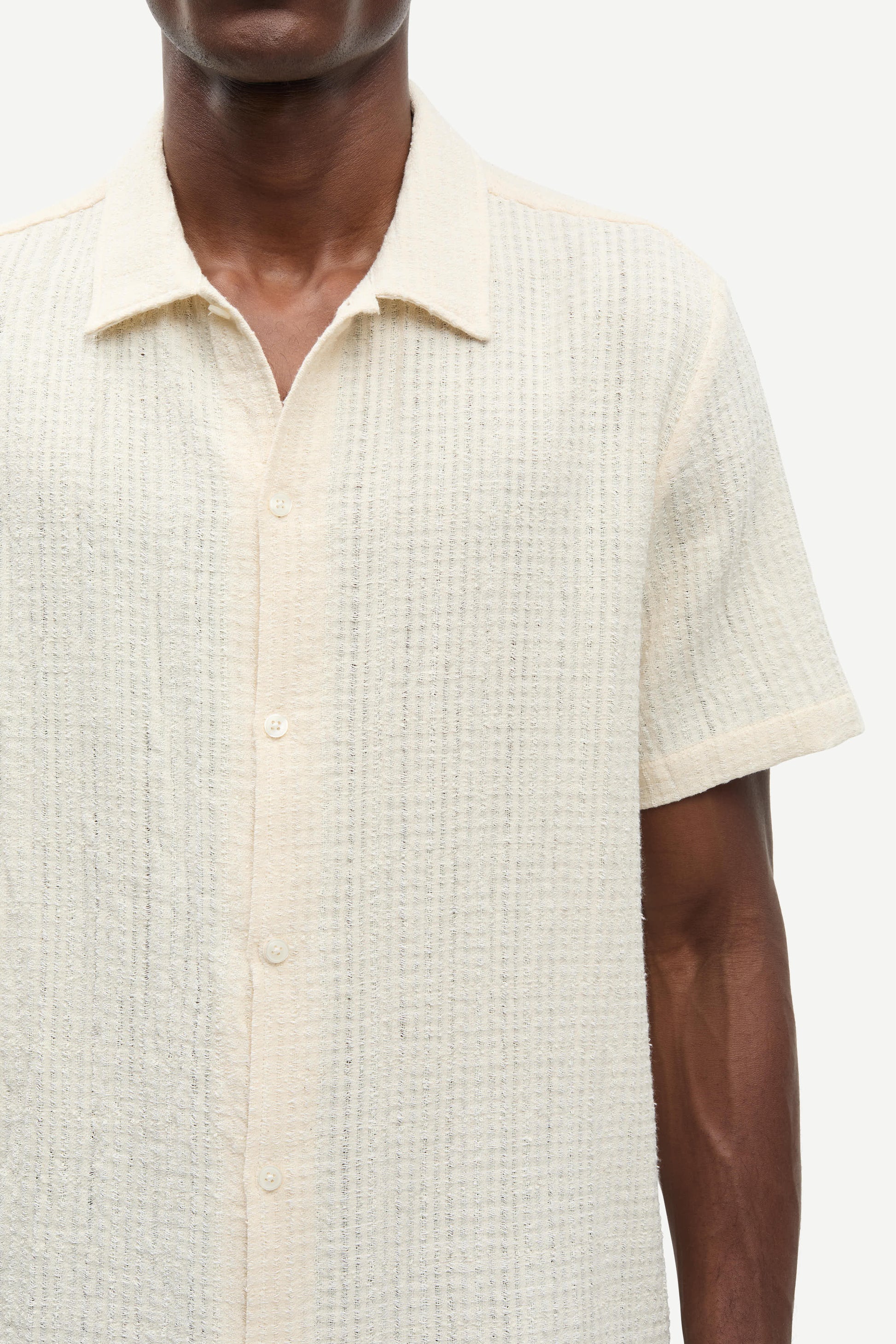 Close-up of a person wearing a textured beige shirt with short sleeves.