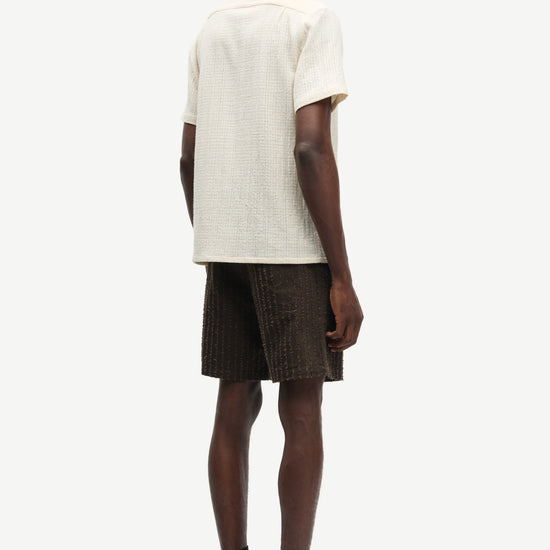 Person wearing a beige shirt and brown shorts on a white background