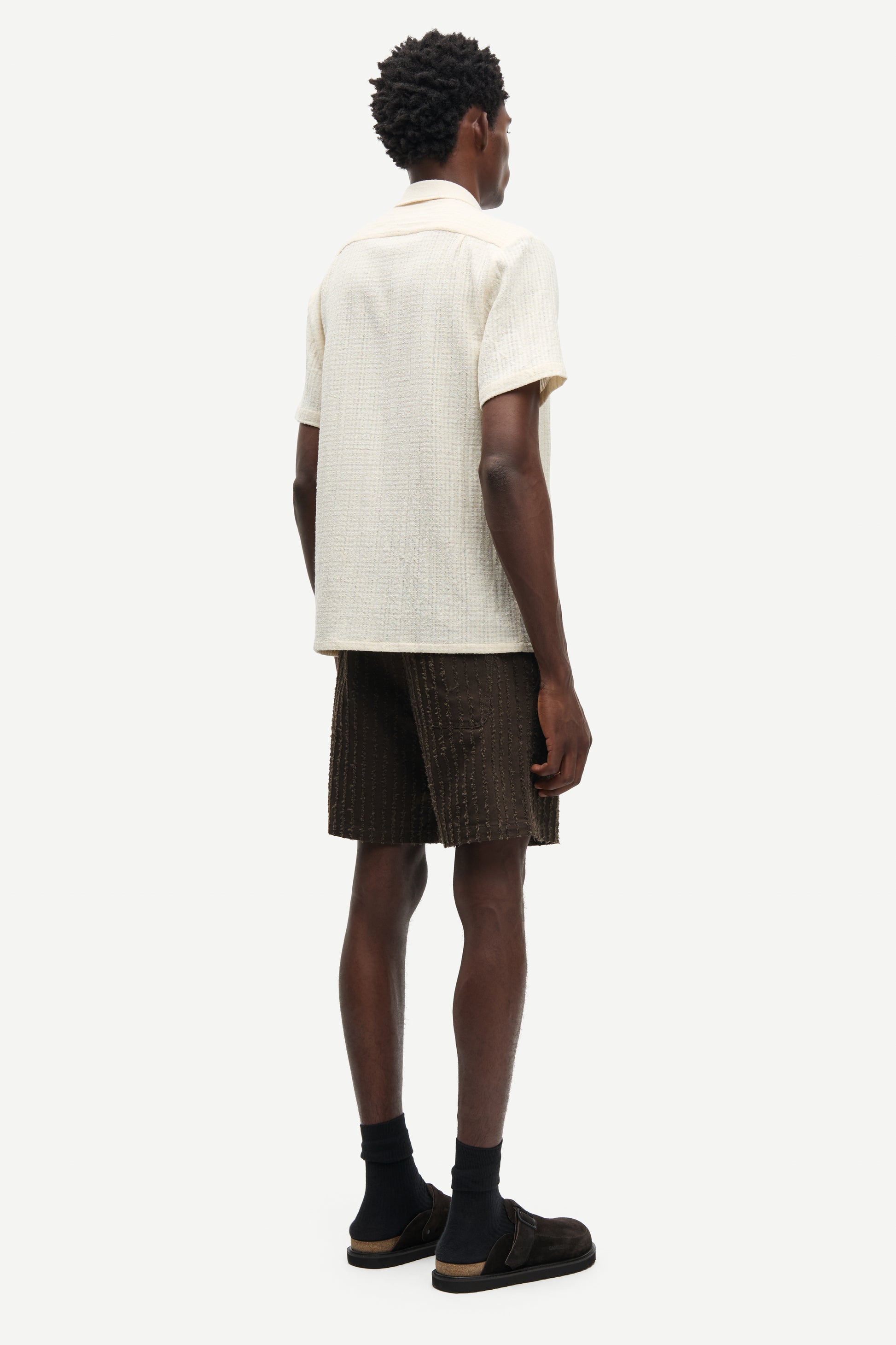 Person wearing a beige shirt and brown shorts on a white background