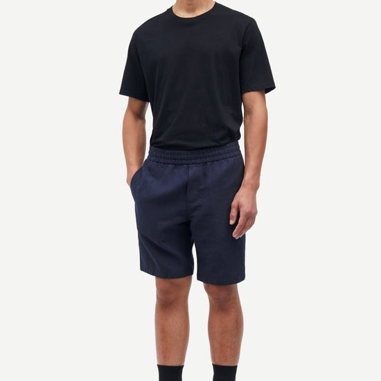 Man wearing a black t-shirt and navy shorts on a white background