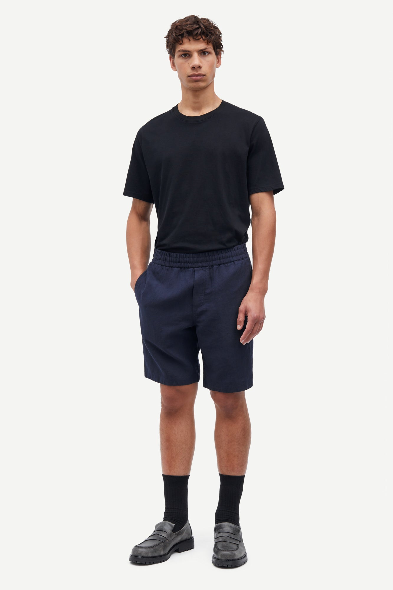 Man wearing a black t-shirt and navy shorts on a white background