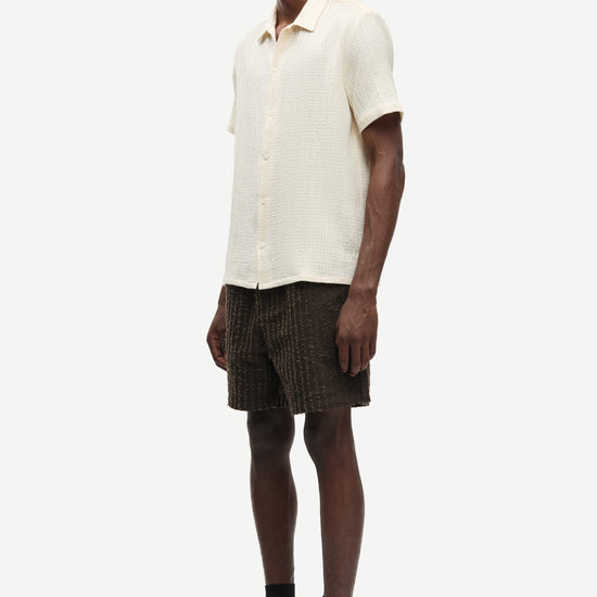 Man wearing a cream shirt and dark shorts on a white background