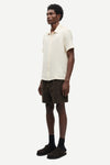 Man wearing a cream shirt and dark shorts on a white background