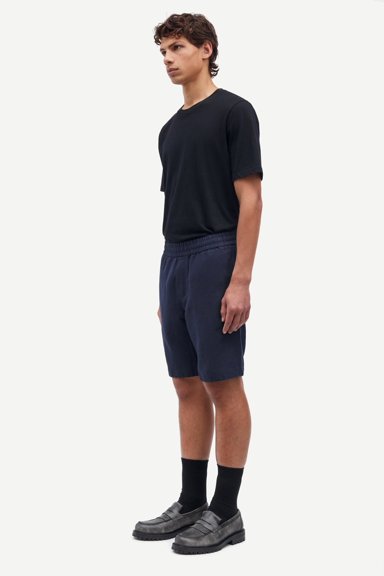 Man wearing a black t-shirt and navy shorts on a white background